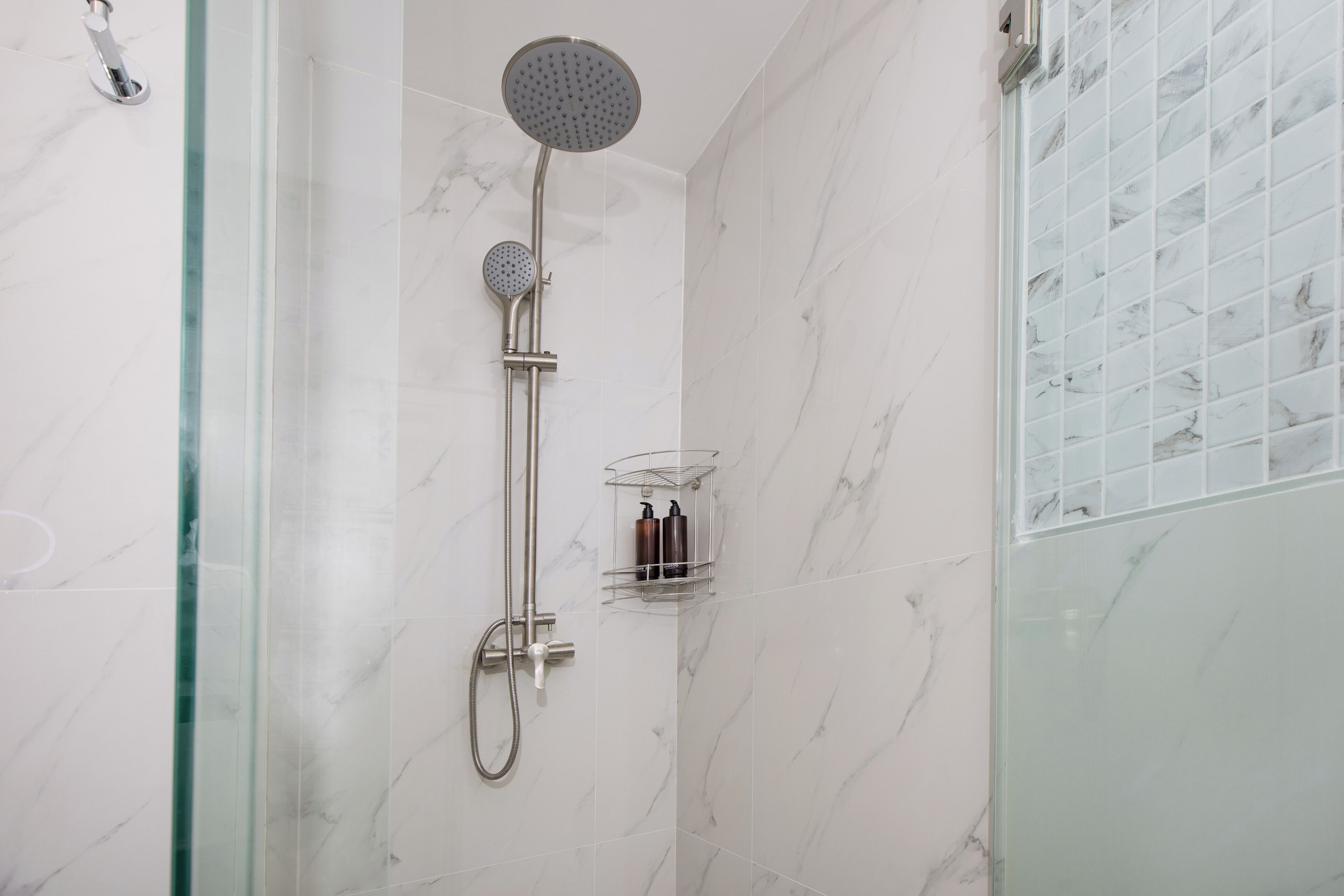 A modern shower with a handheld showerhead and a wall-mounted rain showerhead, a glass shower caddy, and a glass-enclosed shower area.