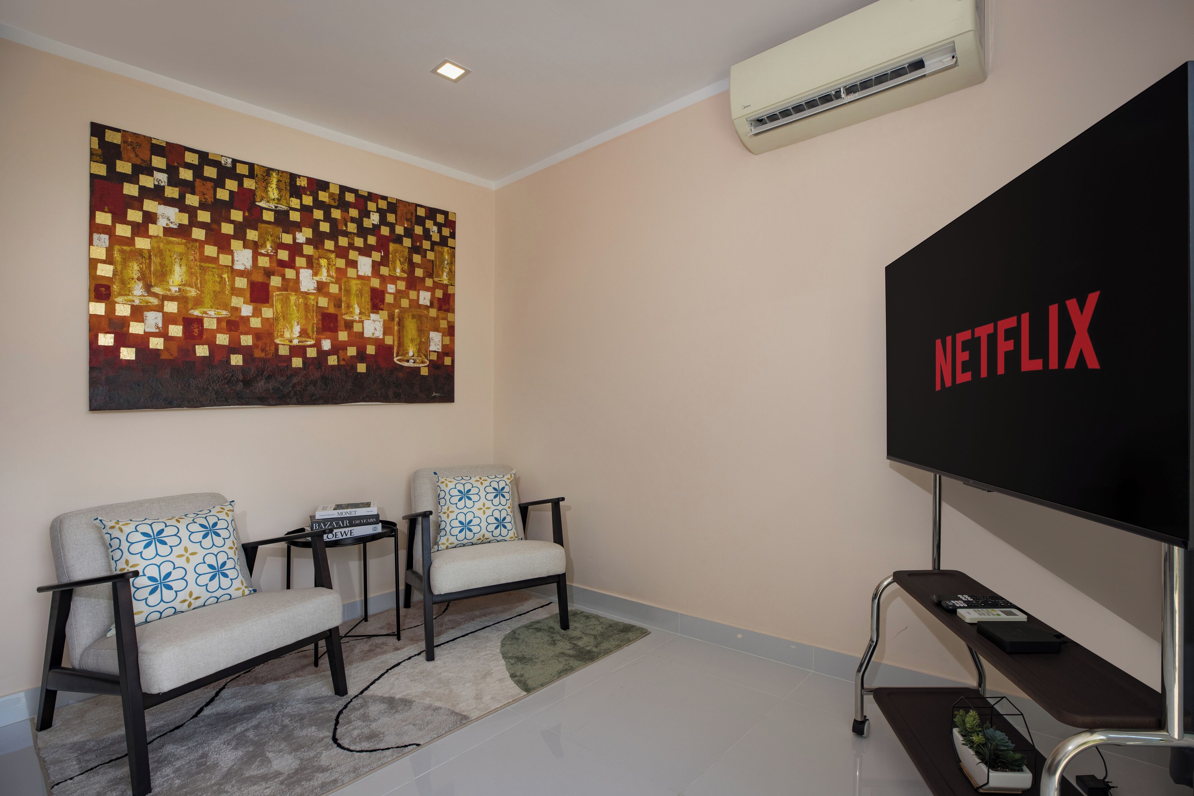 A living room with two armchairs, a coffee table, a flat-screen TV, and a wall-mounted air conditioner.