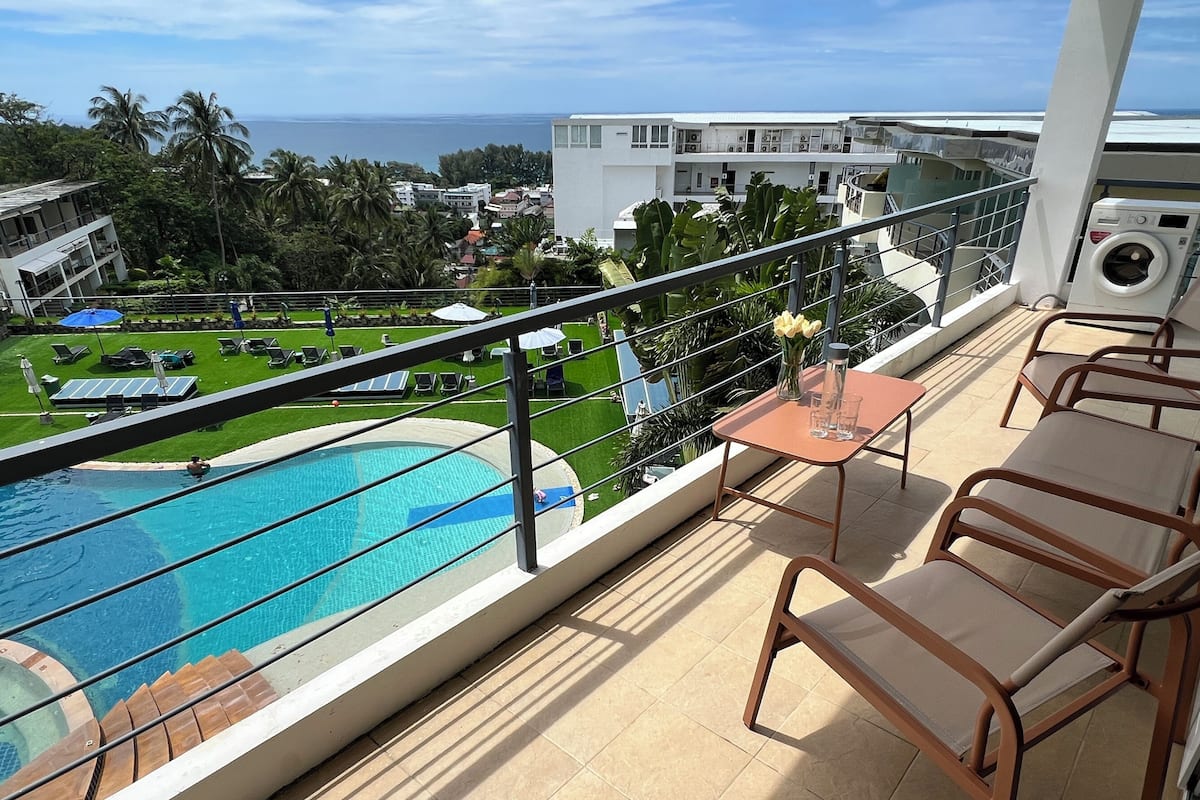 A balcony with a pool, lounge chairs, and a table with a vase of flowers.