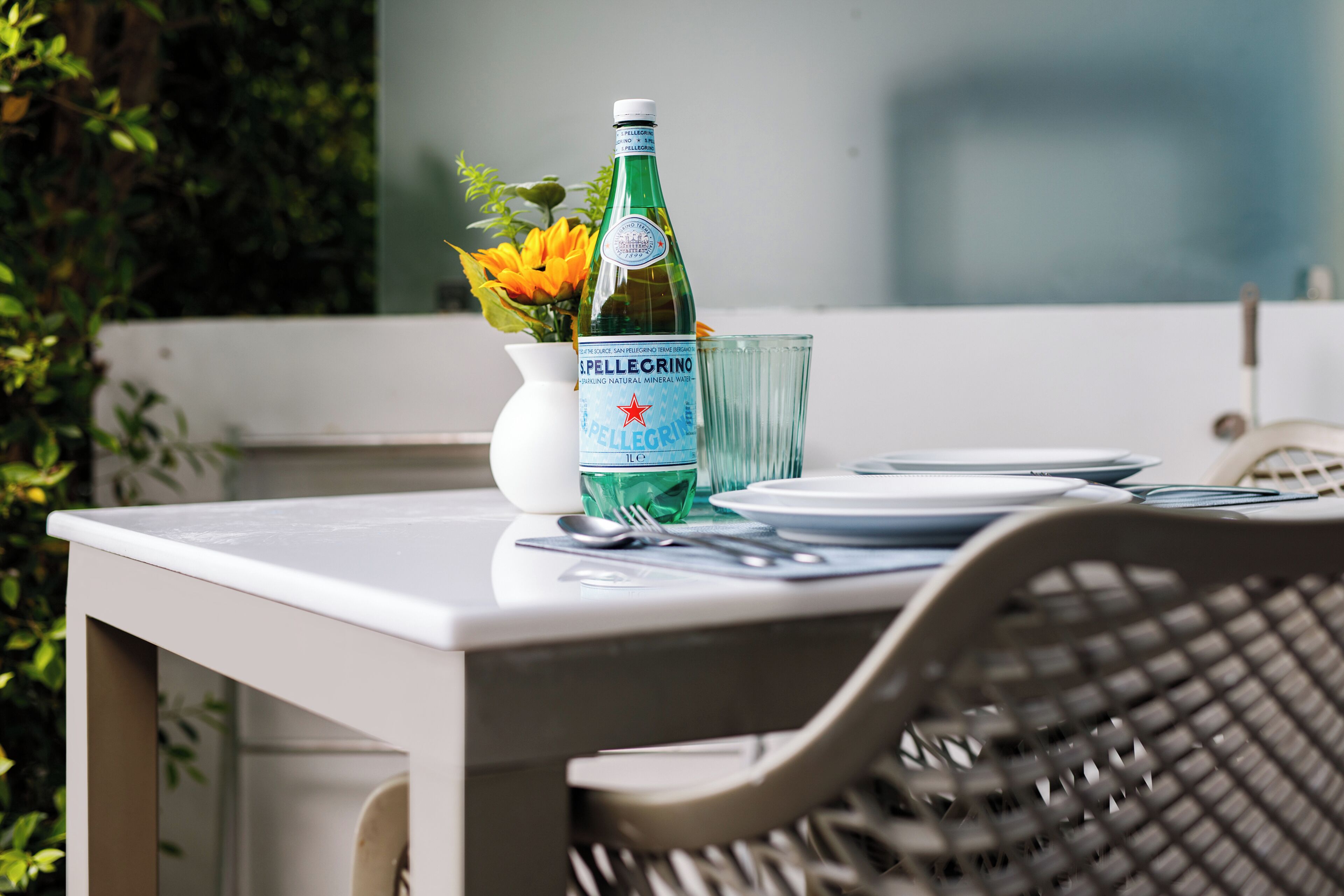 Un tavolo da pranzo con una bottiglia di acqua frizzante Pellegrino, un bicchiere e un vaso con fiori.