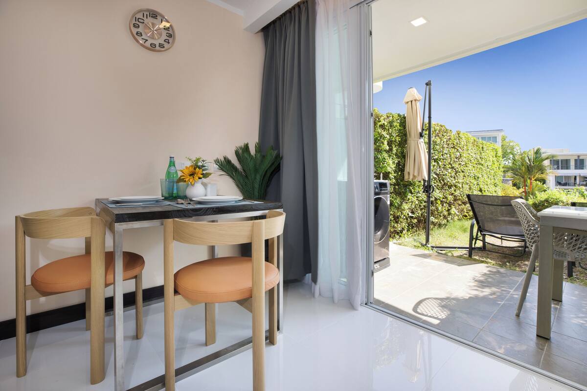 A modern dining area with a table and chairs, a clock on the wall, and a view of the outdoors.