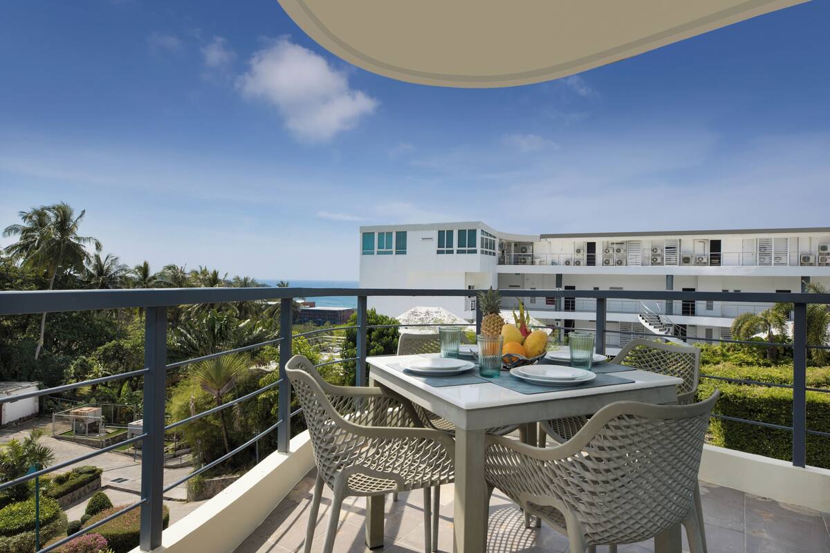 A balcony with a table set for two, overlooking a modern building and a clear sky.