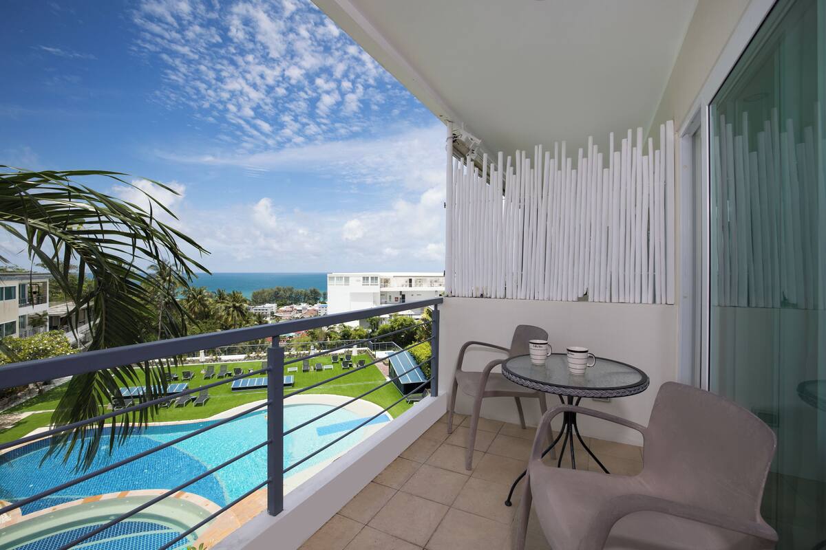 A balcony with a view of a swimming pool, a table with chairs, and a glass partition.