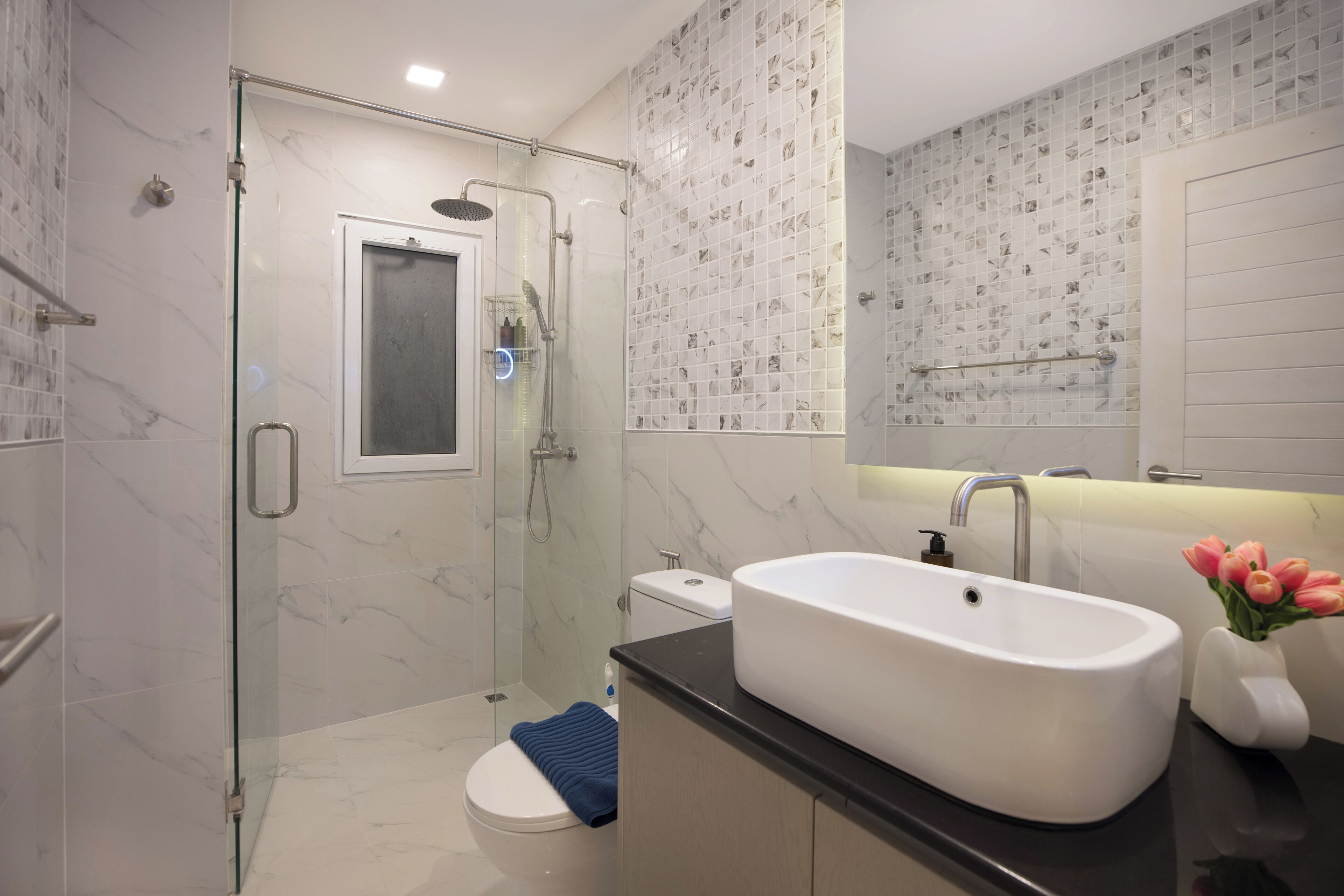 A modern bathroom with a glass-enclosed shower, a white sink, and a toilet.