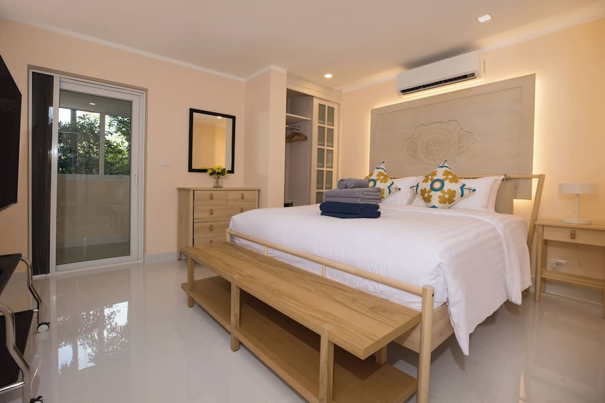 A modern bedroom with a large bed, a bench, a wardrobe, and a mirror.