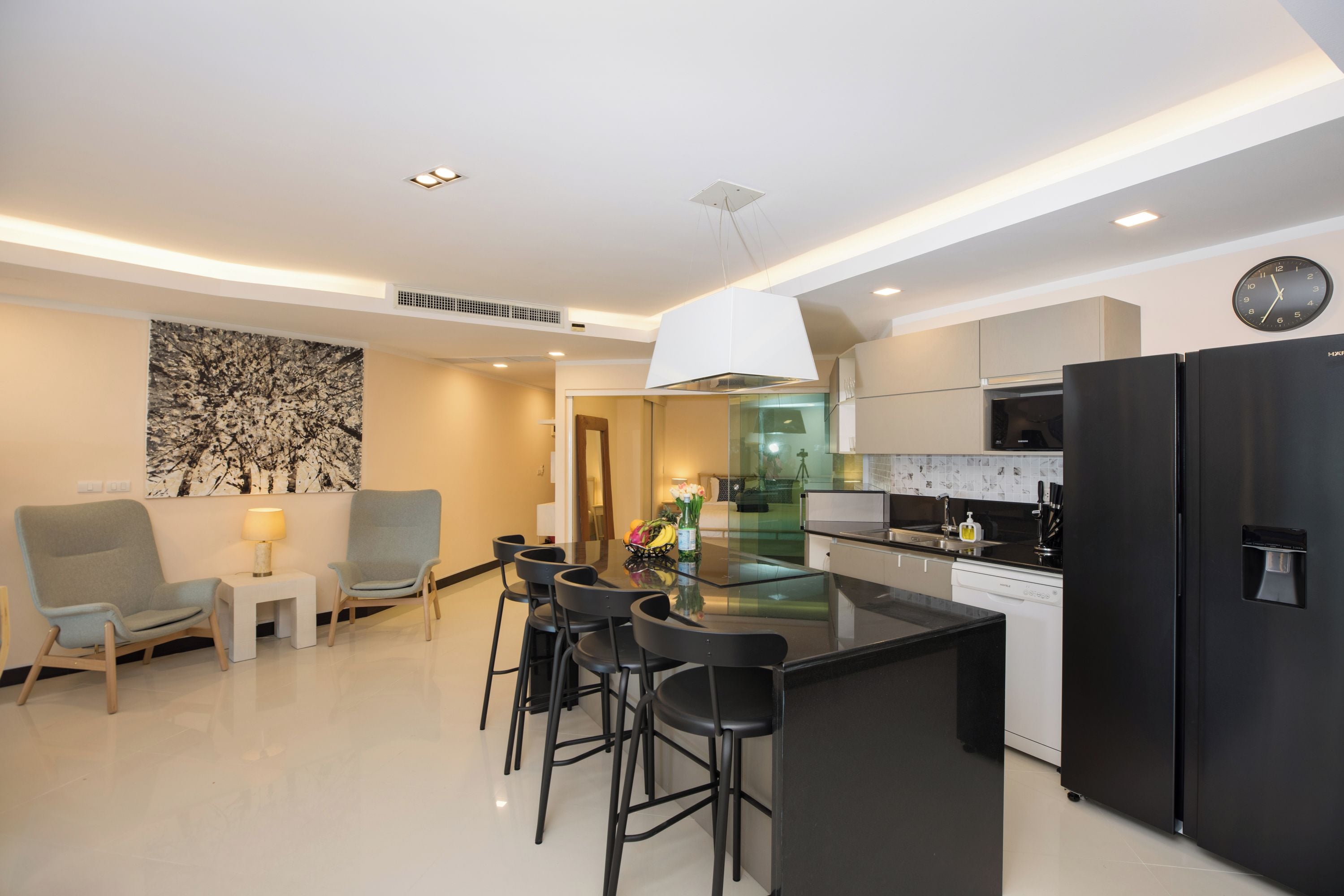 A modern kitchen with a black refrigerator, a dining area with a table and chairs, and a living room with a sofa and a lamp.