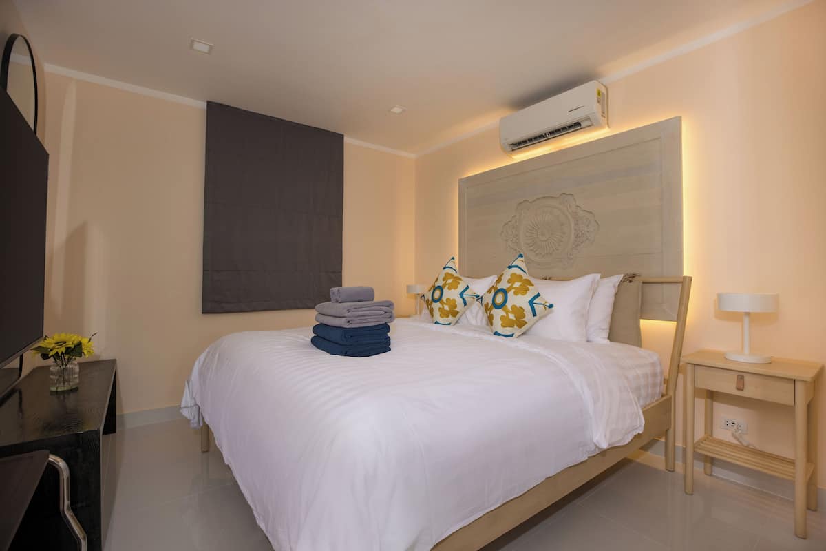 A hotel room with a large bed, a bedside table with a lamp, a TV, and a wall-mounted air conditioner.