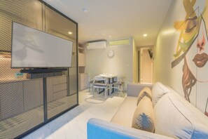 A modern living room with a TV, a dining area, and a sofa. - Woodbridge Property at Karon Butterfly (Karon)