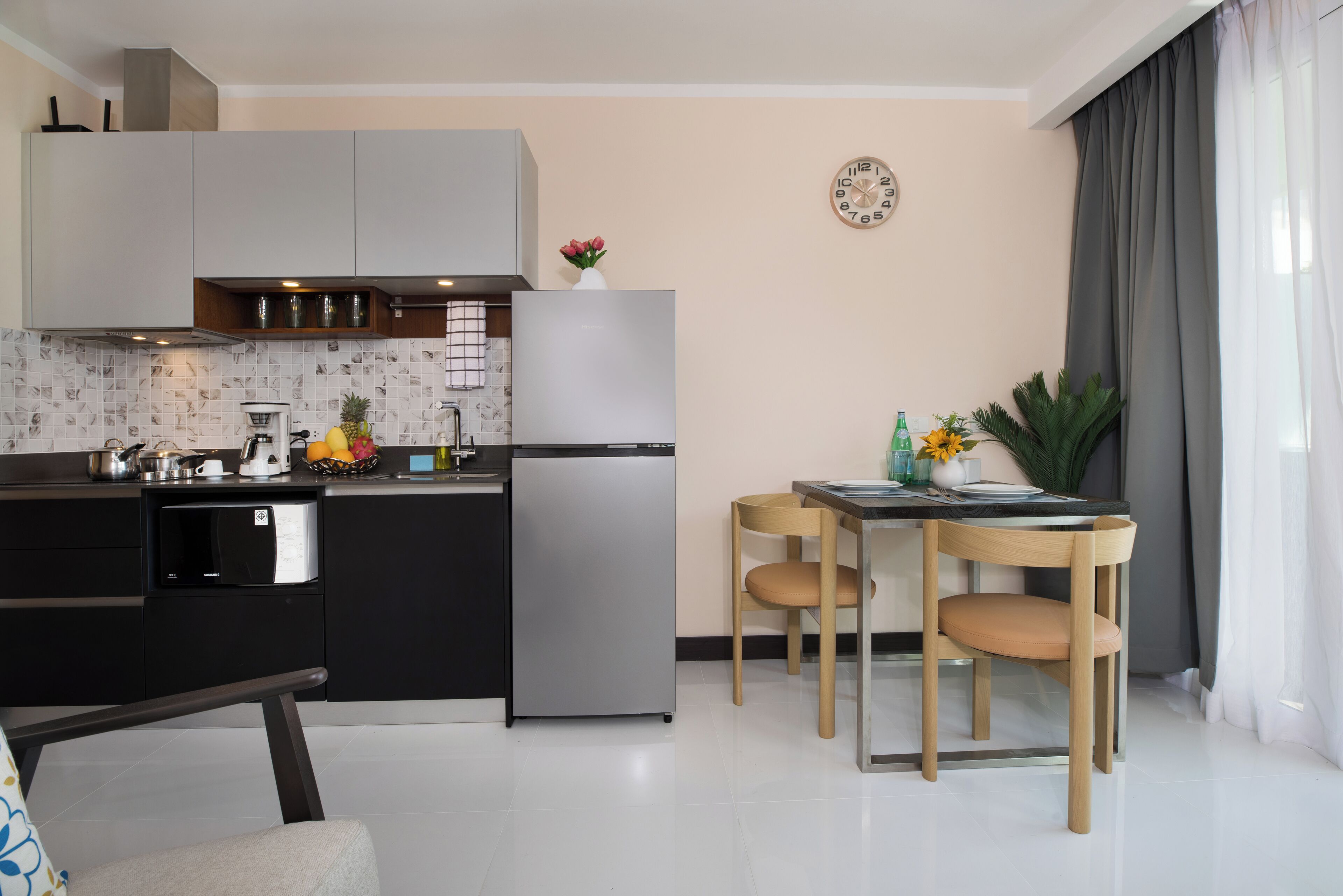 A modern kitchen with a refrigerator, stove, and sink. There is a dining table with chairs and a clock on the wall.