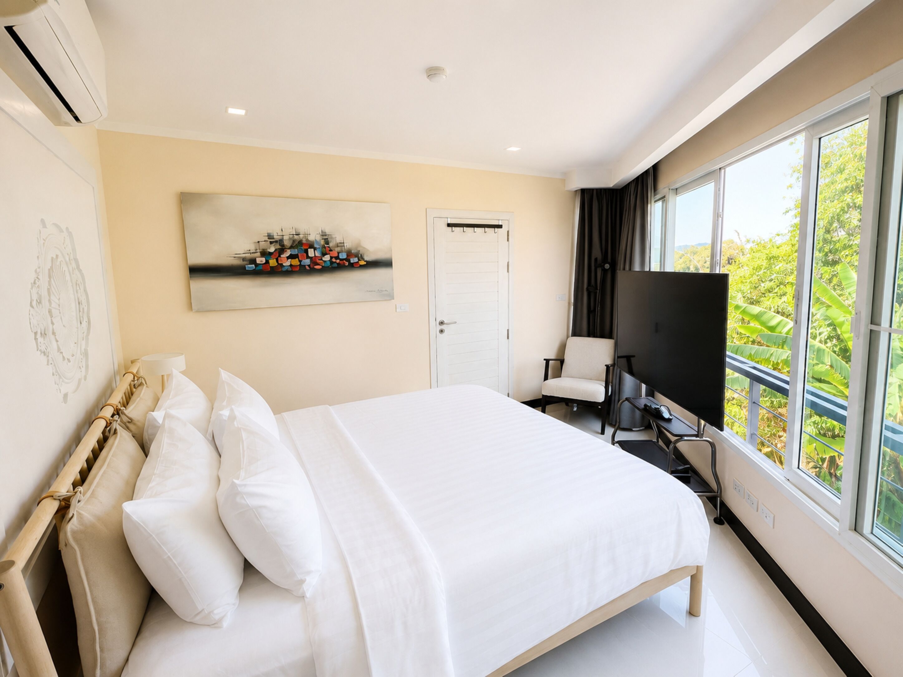 A modern hotel room with a large bed, a television, and a window with a view of greenery.