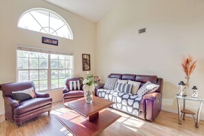 A spacious living room with a large window, leather sofas, a wooden coffee table, and a glass table with decorative items. - Outdoor Kitchen & Gaming Garage: Bradenton Retreat (Bradenton)