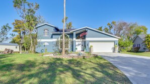 A two-story house with a garage, a front yard with a palm tree, and a clear blue sky. - Outdoor Kitchen & Gaming Garage: Bradenton Retreat (Bradenton)