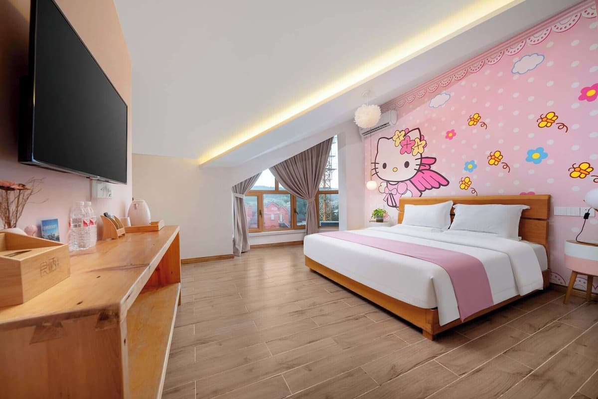 A hotel room with a large bed, a wooden desk, a flat-screen TV, and a window with a view of houses.