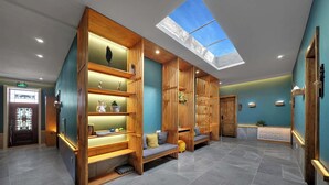 A modern lobby with a skylight, wooden shelving with decorative items, a reception desk, and a seating area.