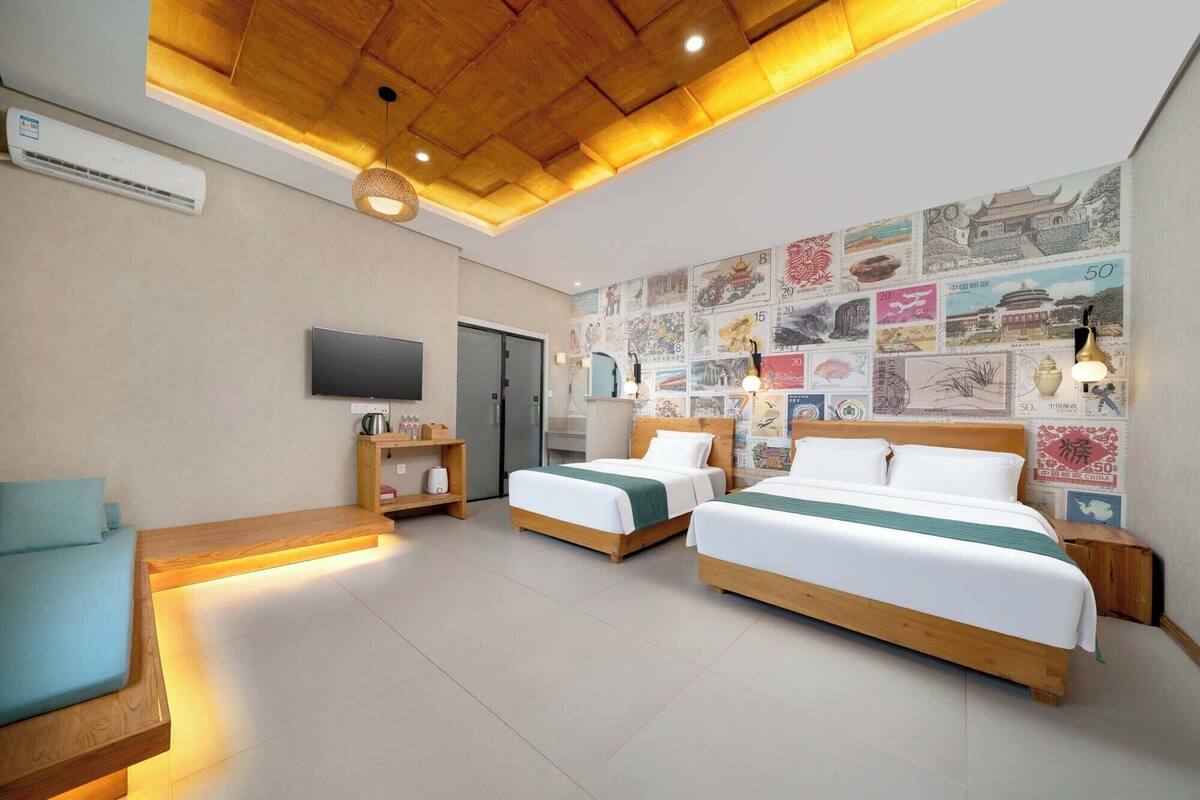 A hotel room with two beds, a TV, a wooden ceiling, and a wall decorated with vintage stamps.