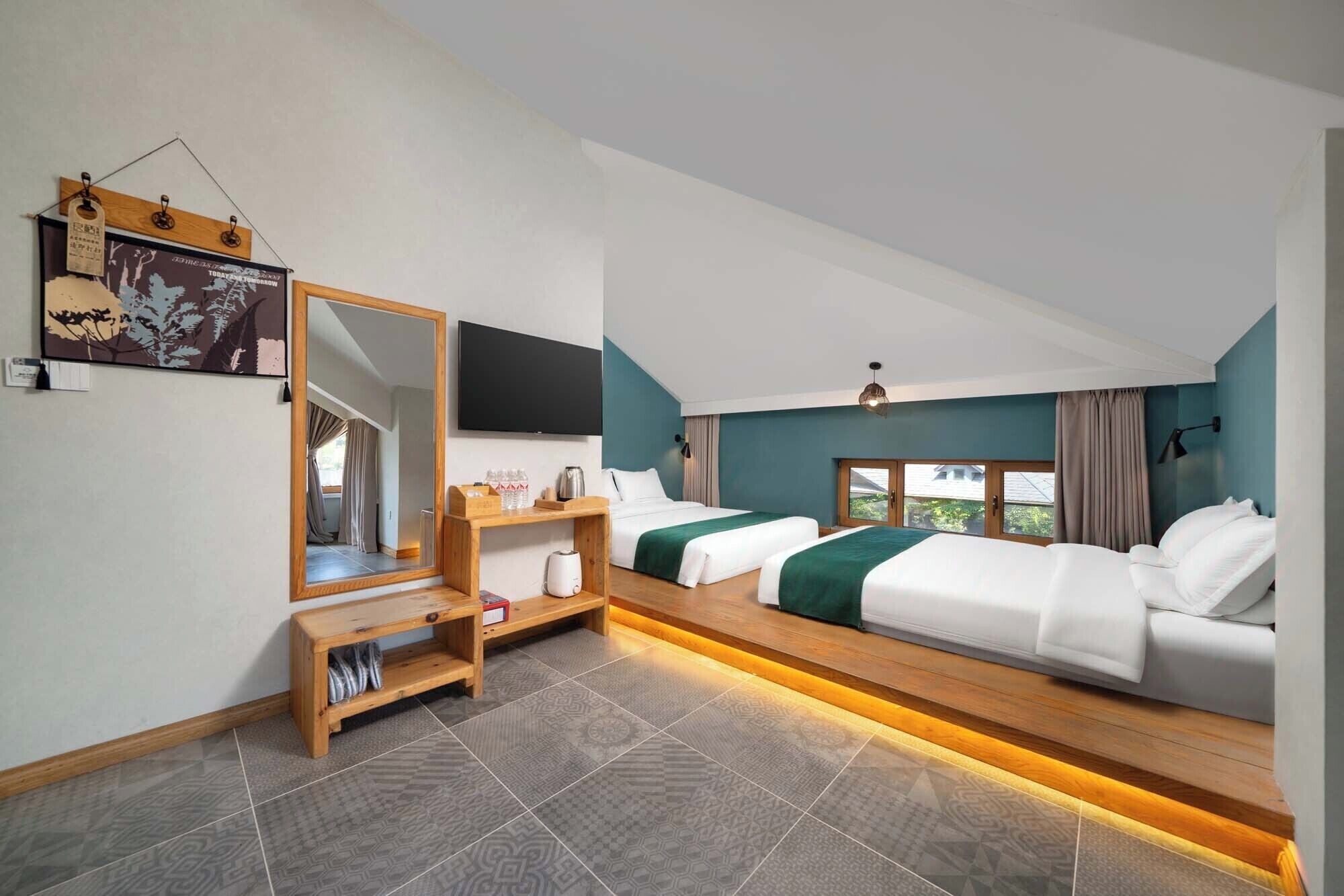 A modern hotel room with two beds, a TV, a wooden bench, and a large mirror.