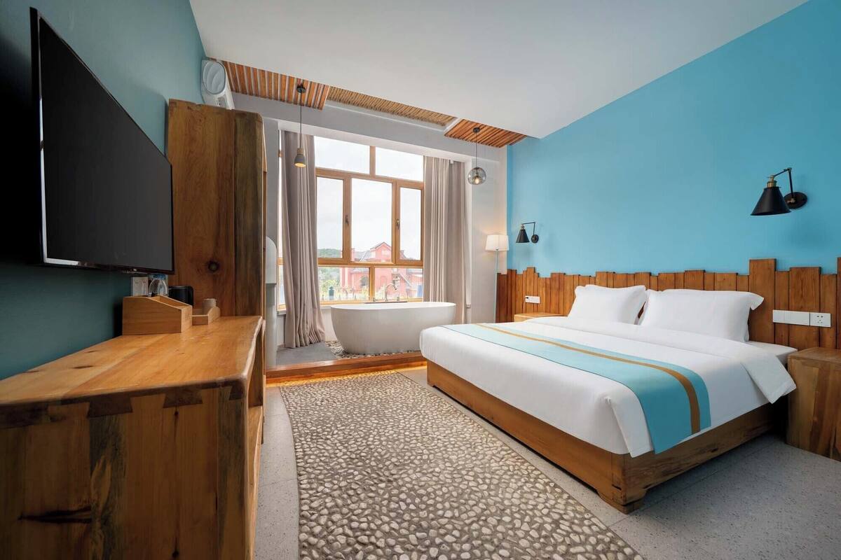 A hotel room with a large bed, a wooden desk, a television, and a window with curtains.