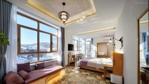 A modern hotel room with large windows, a stone floor, a sofa, a bed, and a desk.