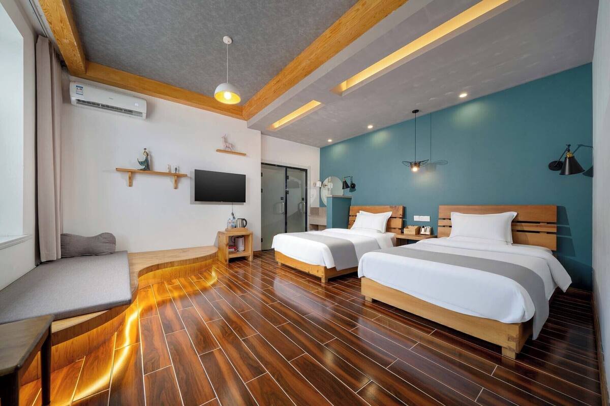 A hotel room with two beds, a TV, a small table, a sofa, and a wooden floor.