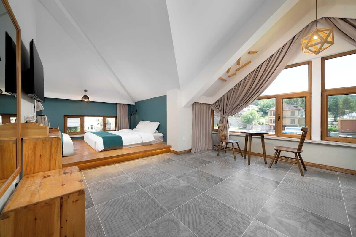 A spacious bedroom with a large bed, a wooden desk, and a dining area.