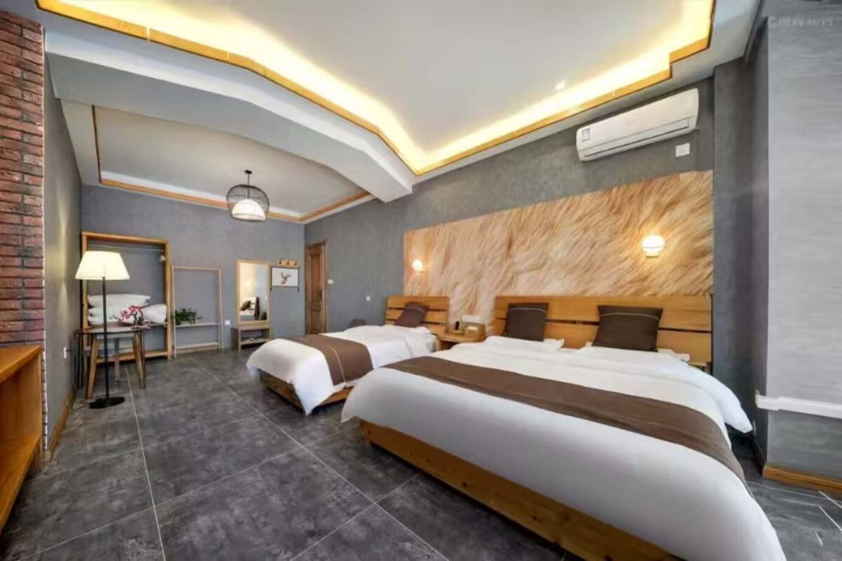 A hotel room with two beds, a desk, a chair, a mirror, and a lamp.