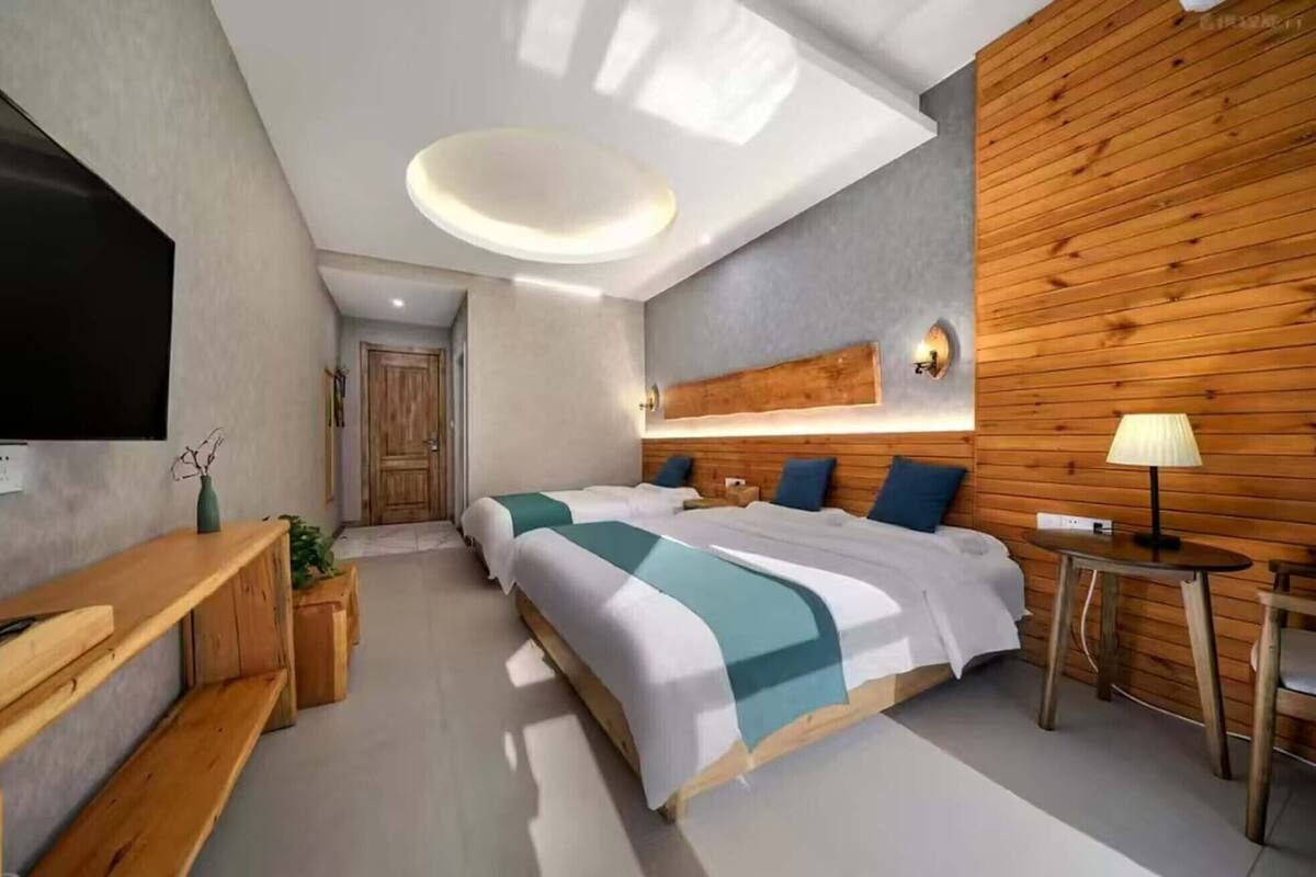 A modern bedroom with a large bed, wooden paneling, a desk, and a TV.