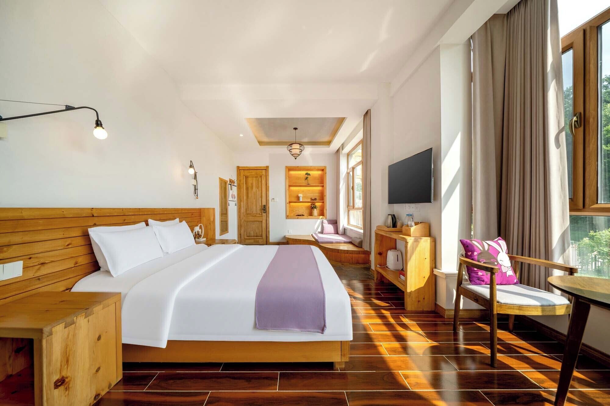 A hotel room with a large bed, a wooden headboard, a desk with a chair, a TV, and a window with curtains.