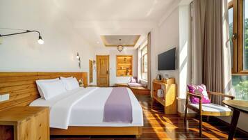 A hotel room with a large bed, a wooden headboard, a desk with a chair, a TV, and a window with curtains.