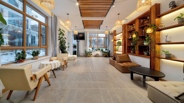 A spacious, well-lit room with large windows, a wooden ceiling, and a variety of seating options including a sofa, chairs, and a bench.