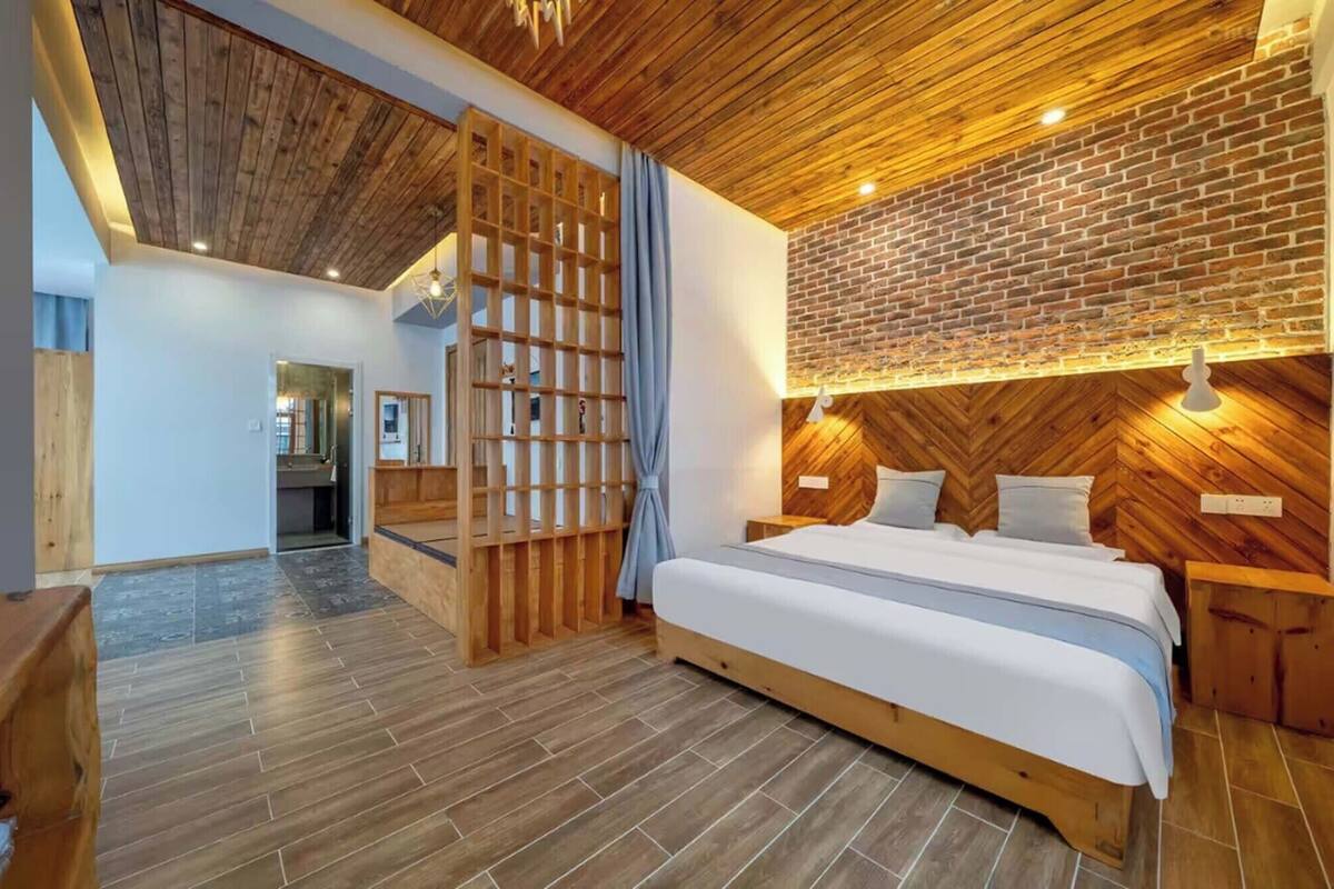 A modern bedroom with a wooden ceiling, a brick accent wall, and a bed with white bedding.