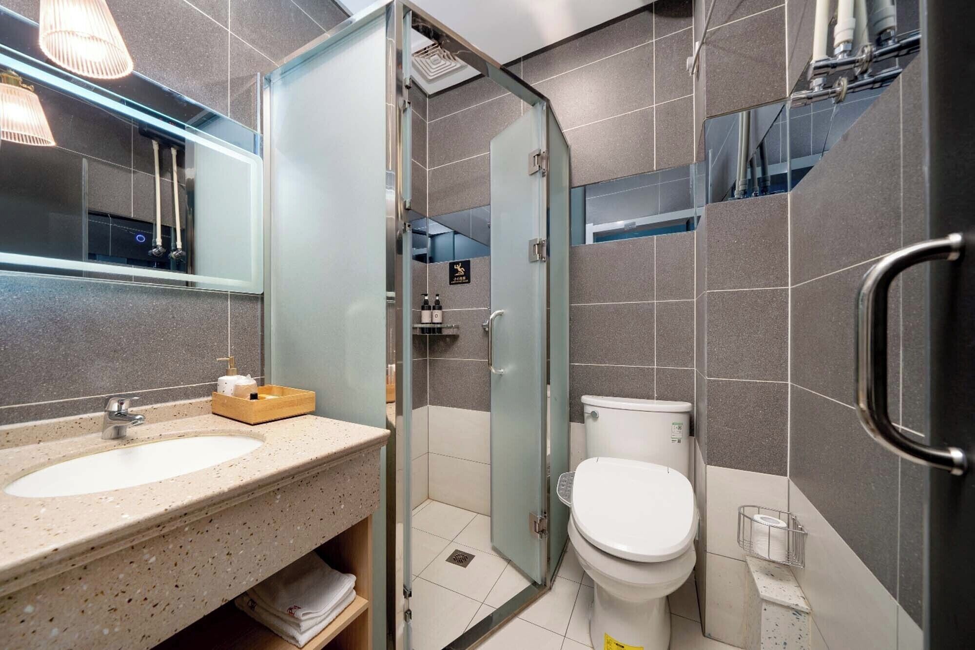 Un baño moderno con cabina de ducha de vidrio, un lavamanos con dispensador de jabón y un inodoro.