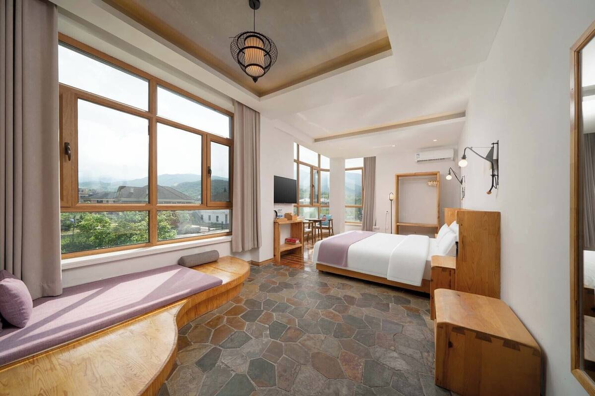 A bedroom with a large window, a bed, a desk, and a seating area.