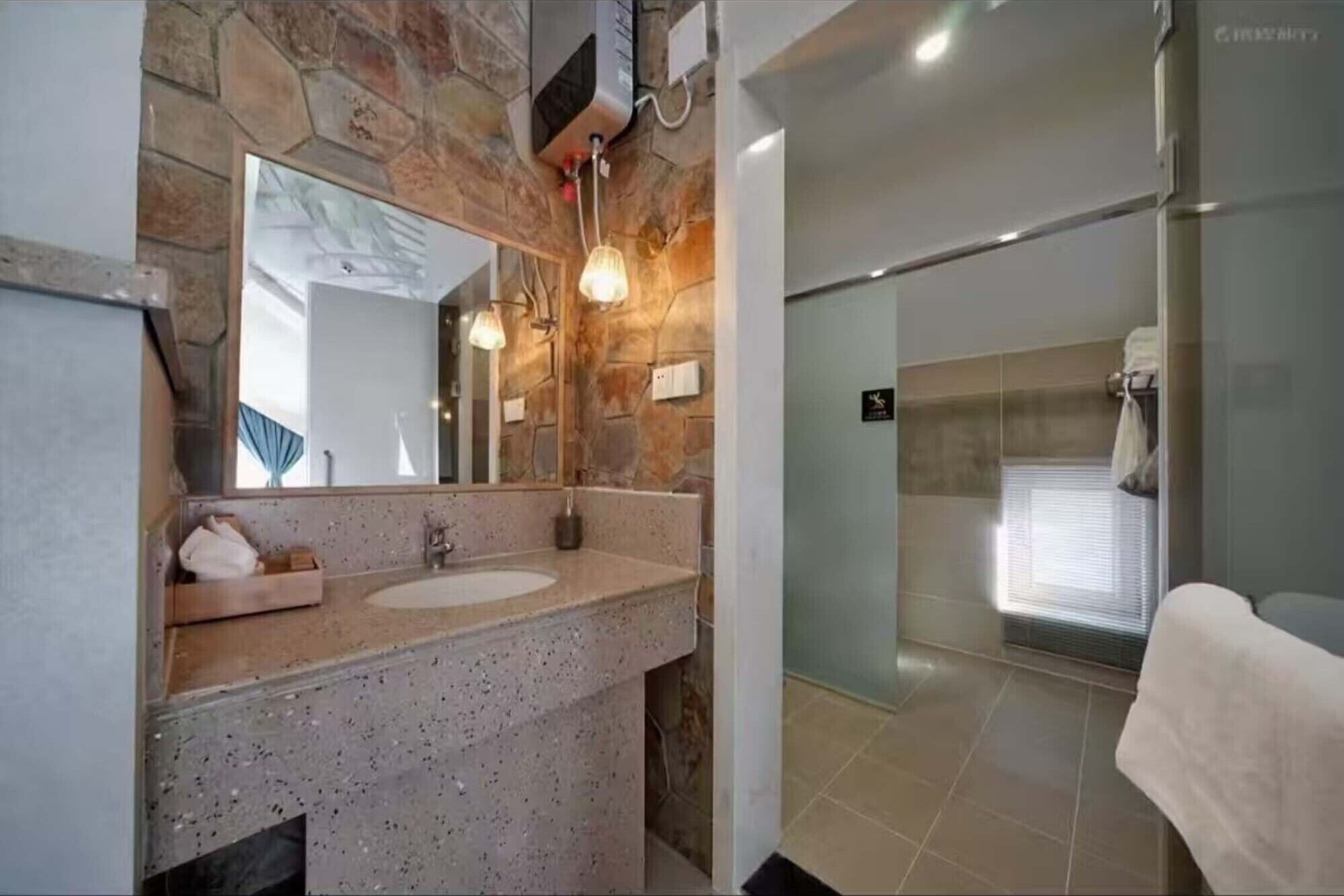 Un baño con pared de piedra, un espejo grande, un lavamanos y una zona de ducha.