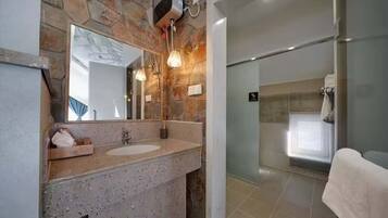 Un baño con pared de piedra, un espejo grande, un lavamanos y una zona de ducha.