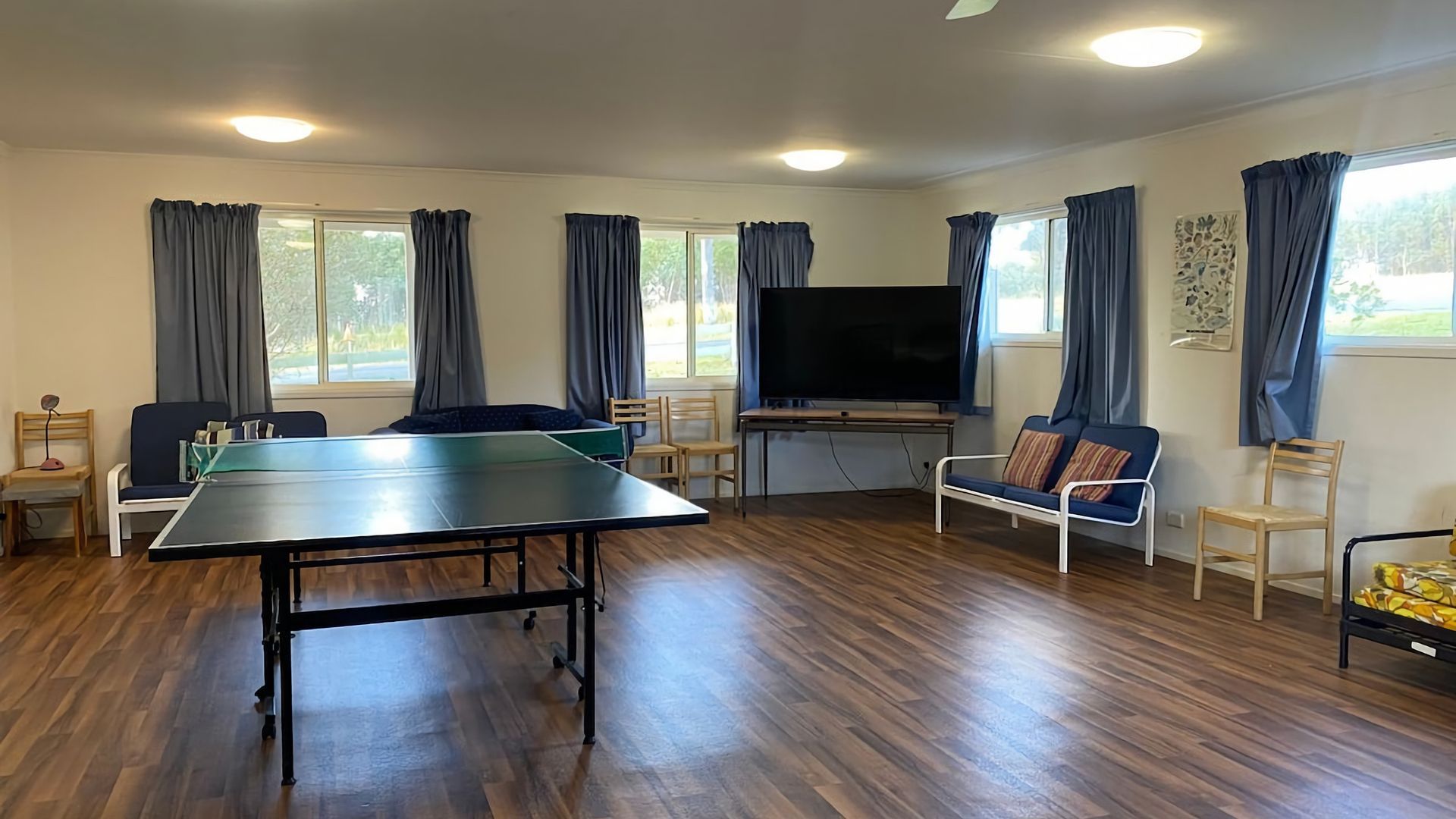 A room with a ping pong table, a television, and seating.