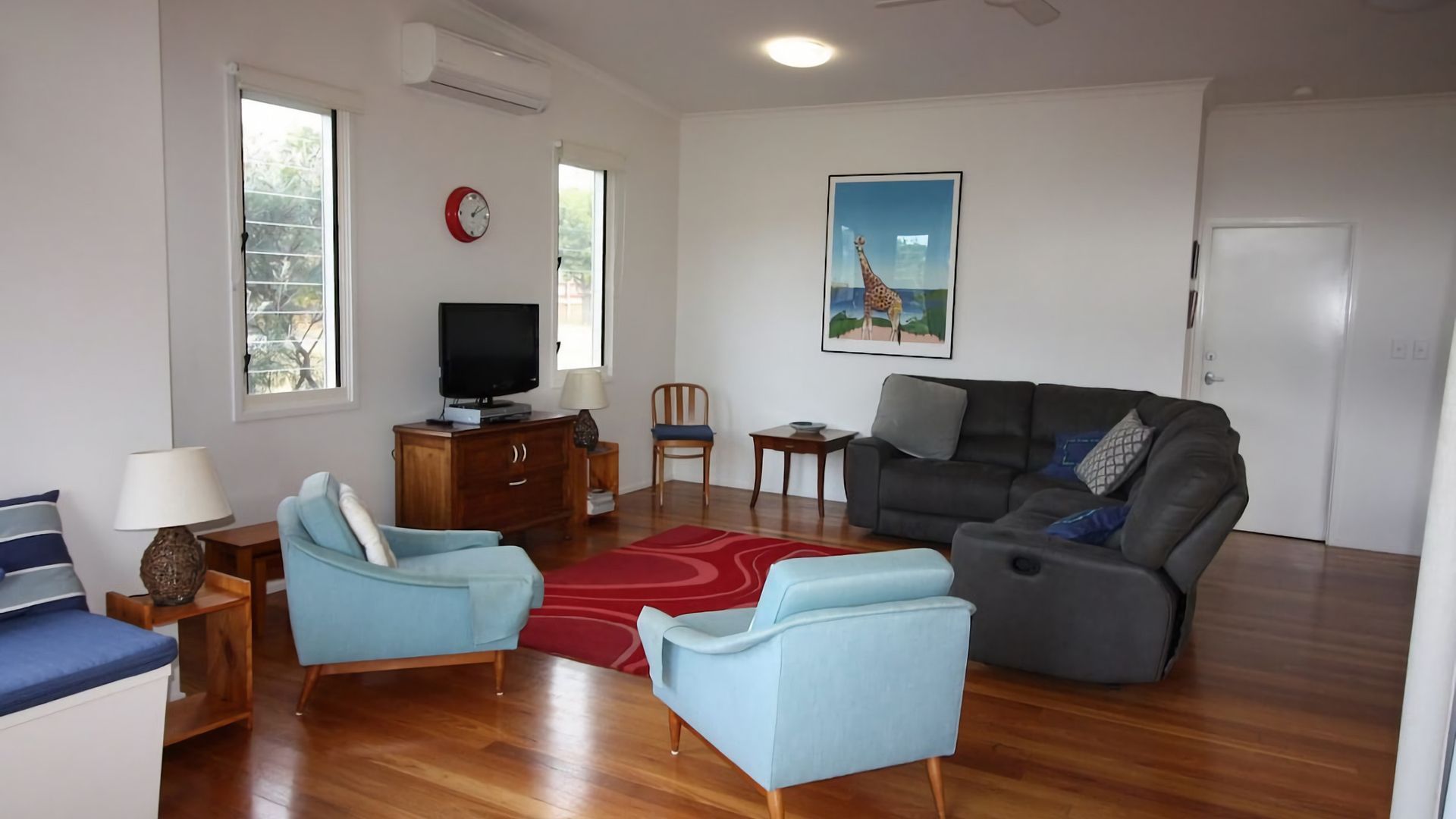 A living room with a sofa, two armchairs, a television, a clock, and a painting on the wall.