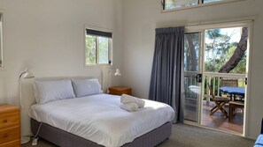A bedroom with a bed, bedside lamps, a wooden nightstand, and a view of an outdoor deck. - Andagen has water glimpses (Bendalong)