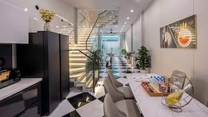 A modern kitchen with a black refrigerator, a dining table with chairs, and a staircase leading to an upper level. - Mei's house homestay (Da Nang)