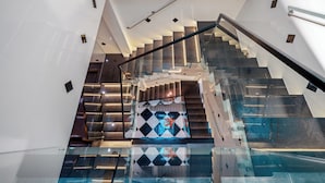 A modern staircase with glass railings and a geometric patterned wall. - Mei's house homestay (Da Nang)
