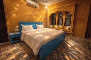 A room with a large bed, a nightstand, a bench with cushions, and a wall-mounted air conditioner. - Mayra Boutique Casa (Jaisalmer)