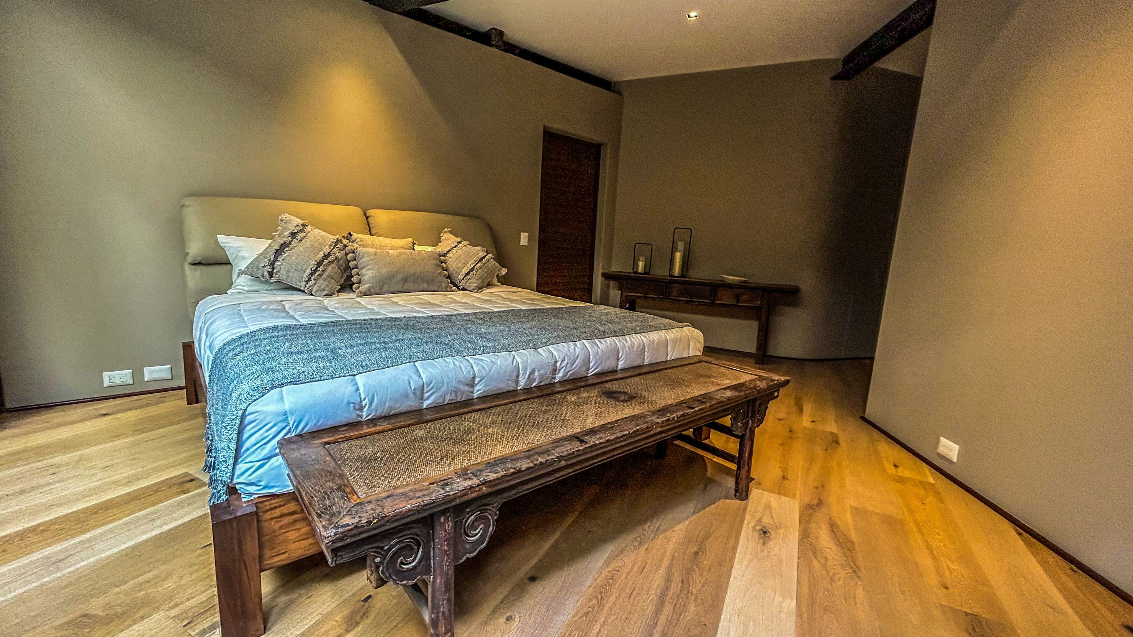 A bedroom with a large bed, a wooden bench, and a small table.