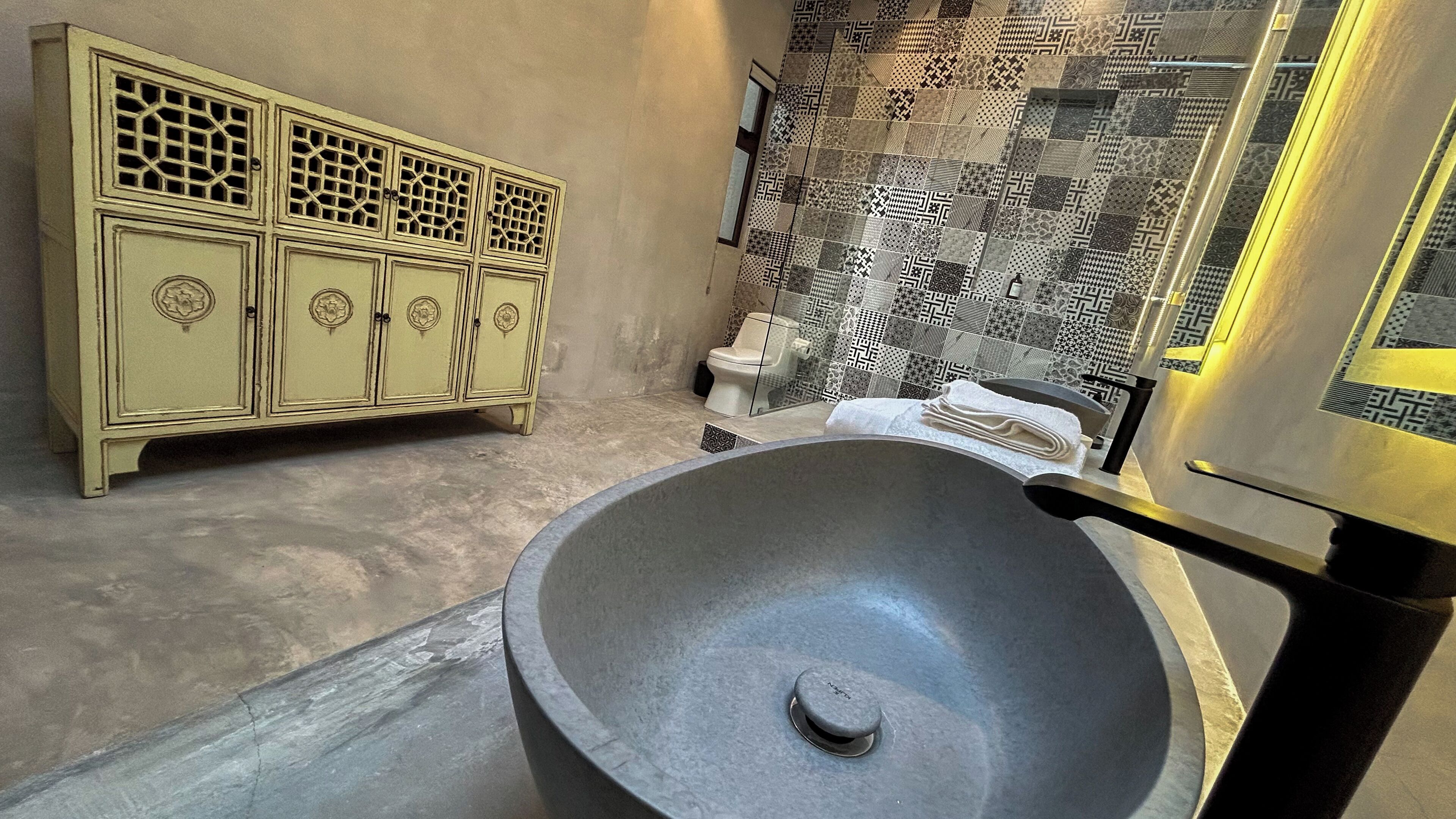 A bathroom with a large stone basin, a vintage cabinet, and patterned tiles.