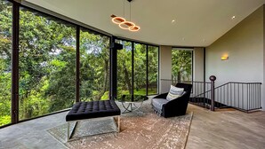 A spacious room with large windows, a black sofa, a chair, and a round table.