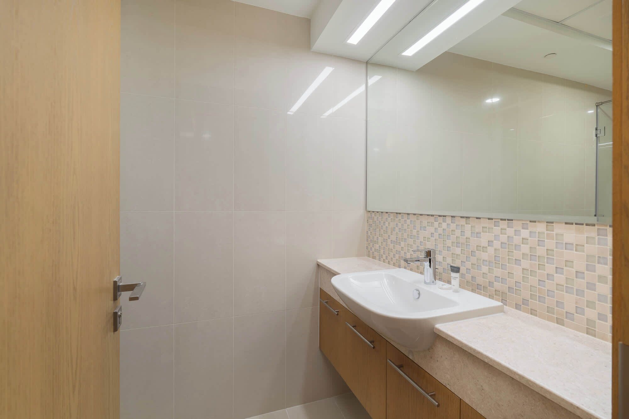 A modern bathroom with a large mirror, a sink, and wooden cabinets.