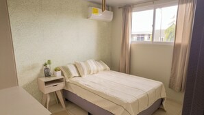 A bedroom with a bed, a bedside table, a small desk, and a window with curtains.