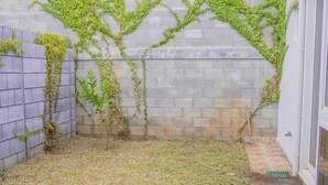 A small, enclosed outdoor area with a brick wall, a tiled floor, and some greenery growing on the wall.