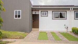 Ein modernes, zweistöckiges Haus mit grauem Anstrich, einer Haustür und einem kleinen Garten mit Rasen und einem gepflasterten Weg.