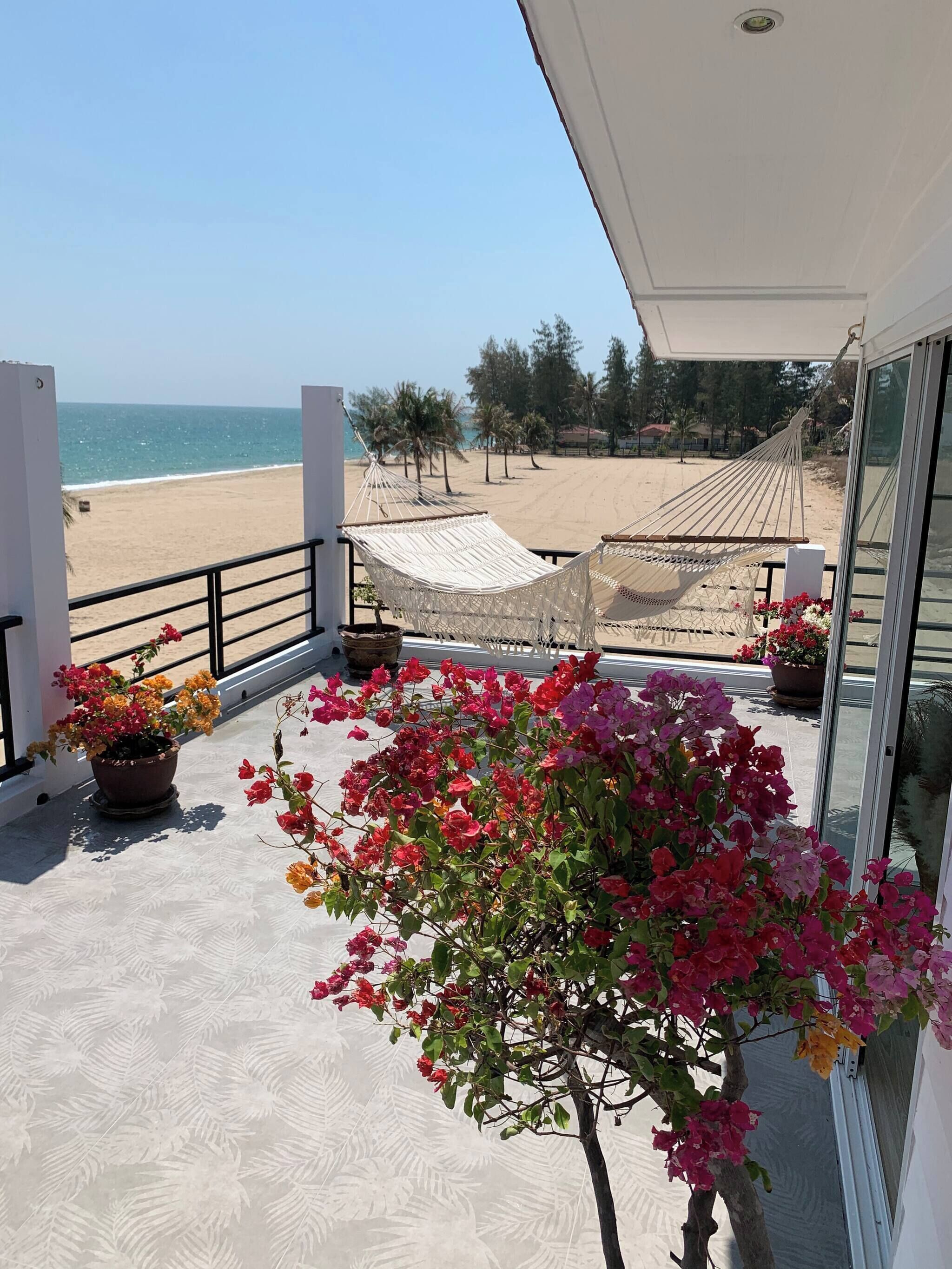 A balcony with a view of the beach, a hammock, and potted plants.