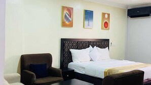 A hotel room with a bed, two armchairs, a small table, and three wall art pieces. - New Benny Rose   (Abuja)