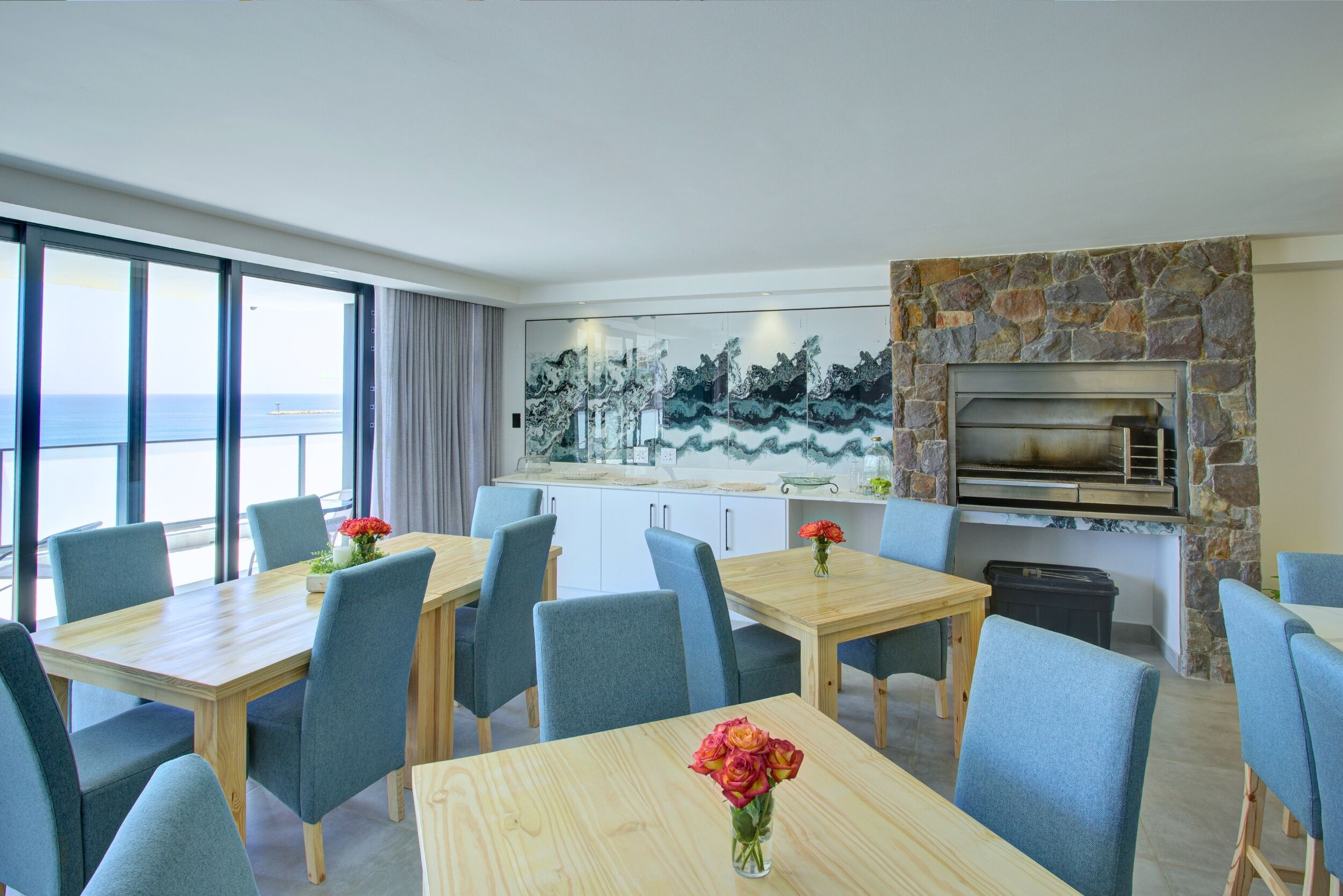 A dining area with a stone fireplace, large windows with a view, and blue upholstered chairs.